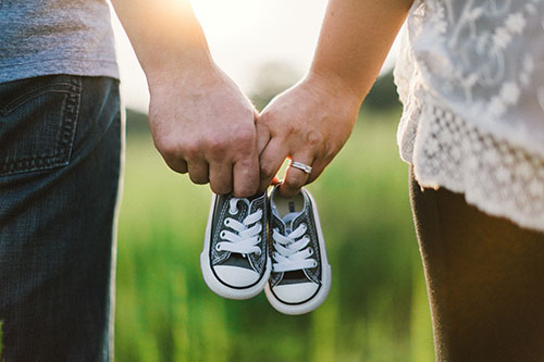 Couple holding hands and baby shoes